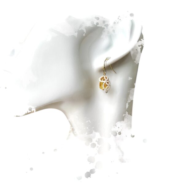 Boucles d'oreilles Honey en acier inoxydable plaqué or, deux perles d'ambre piedbald naturel avec un motif en fil blanc fait main selon la technique de la frivolité.