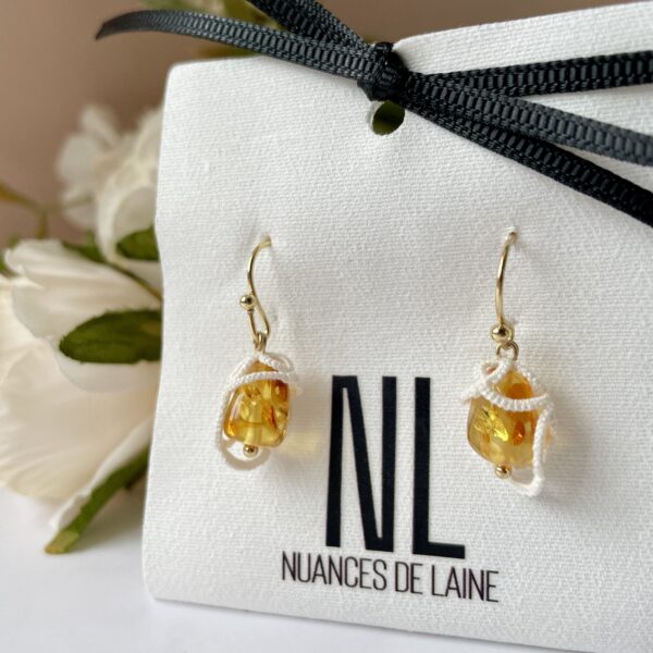 Boucles d'oreilles Honey en acier inoxydable plaqué or, deux perles d'ambre piedbald naturel avec un motif en fil blanc fait main selon la technique de la frivolité.